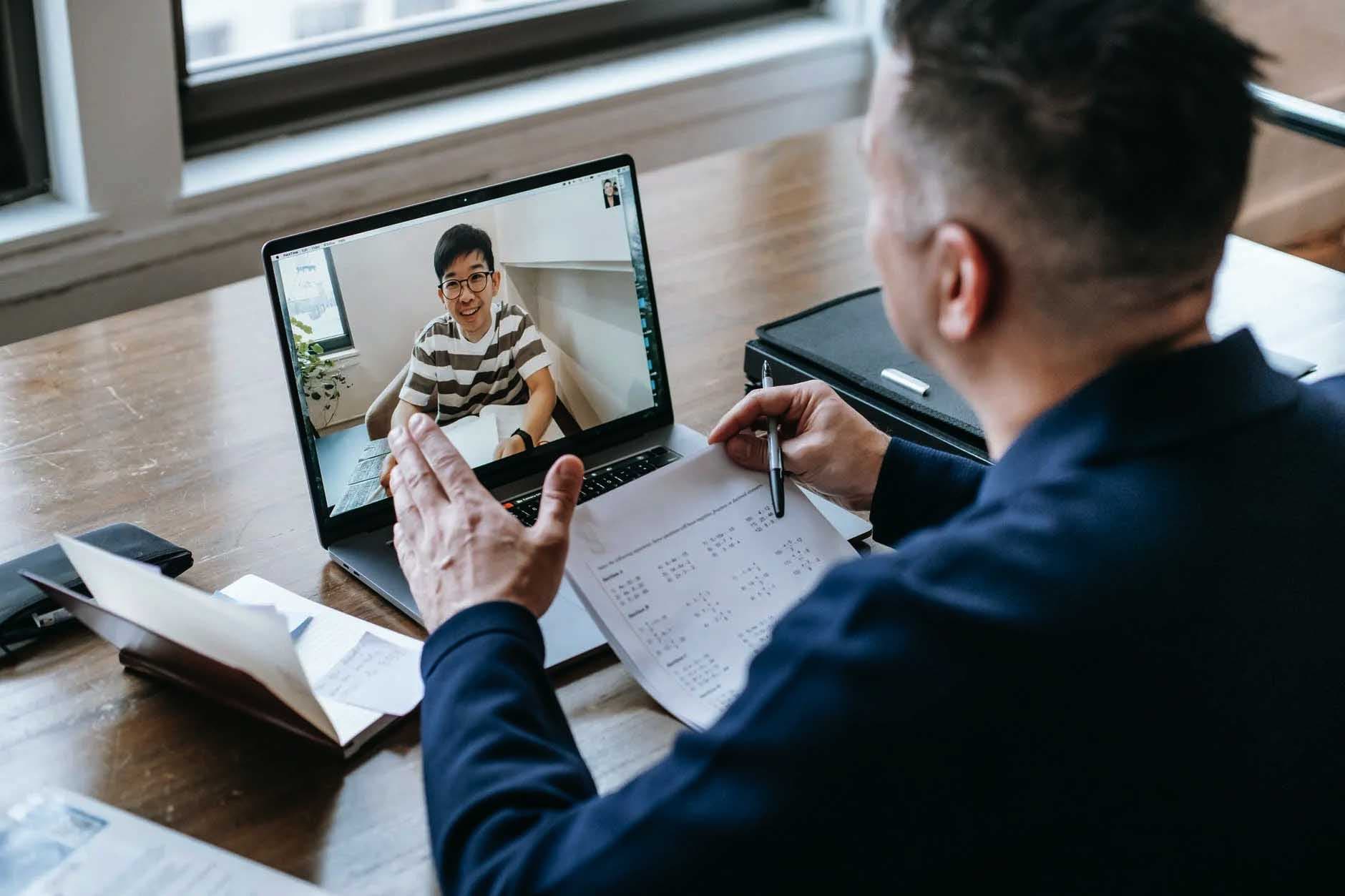 Instructor teaching an online course from home using a laptop with a student on video call
